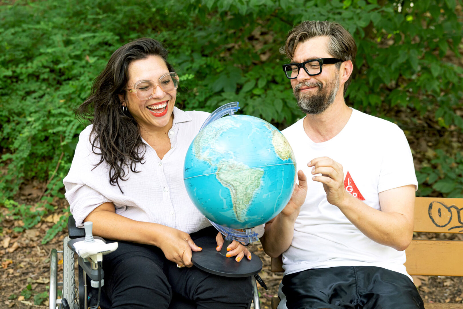 Kim und David sitzen lachend im Park und halten gemeinsam einen Globus.