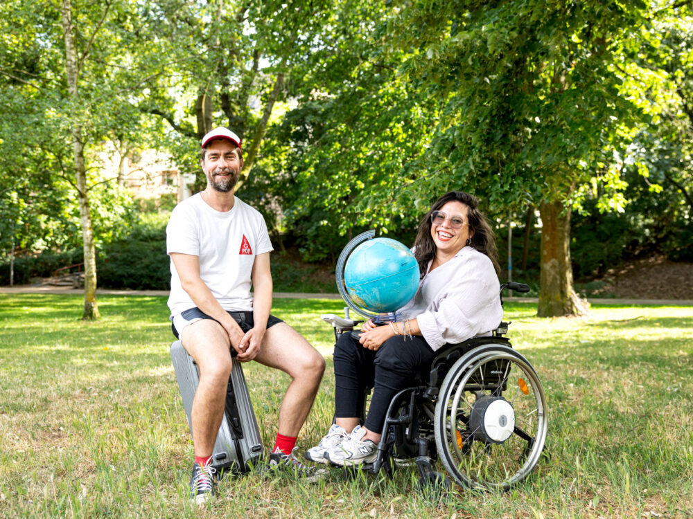 David steht neben Kim im Rollstuhl auf einer Wiese, sie halten einen Globus.